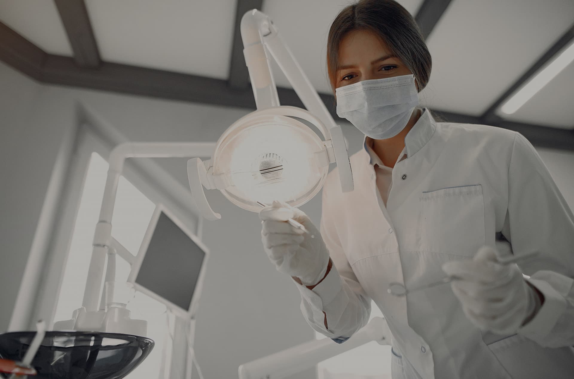 Dentist in a mask adjusting the dental light before treatment